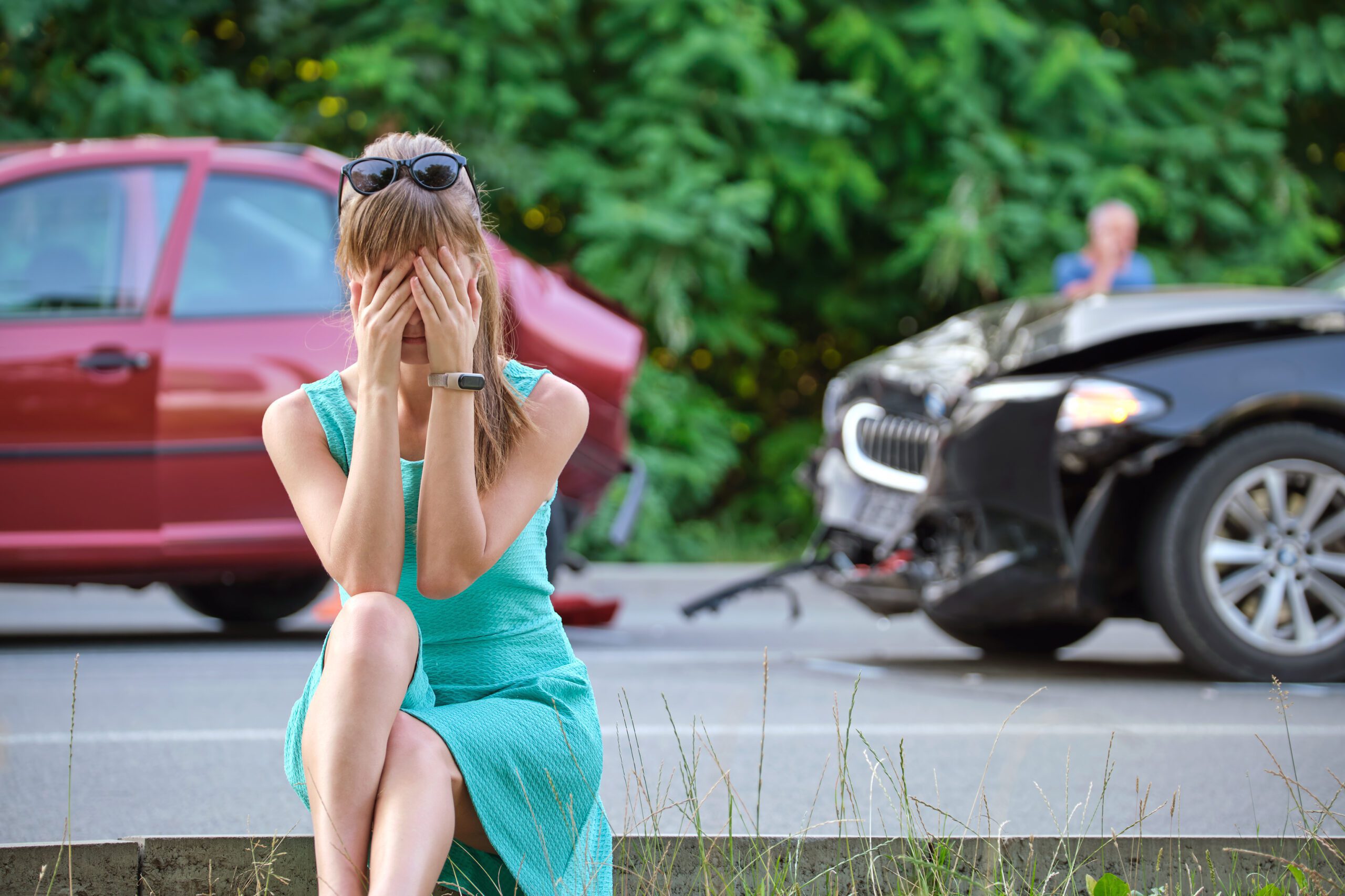 woman sitting on the side of the road with her head in her hands following a serious car accident