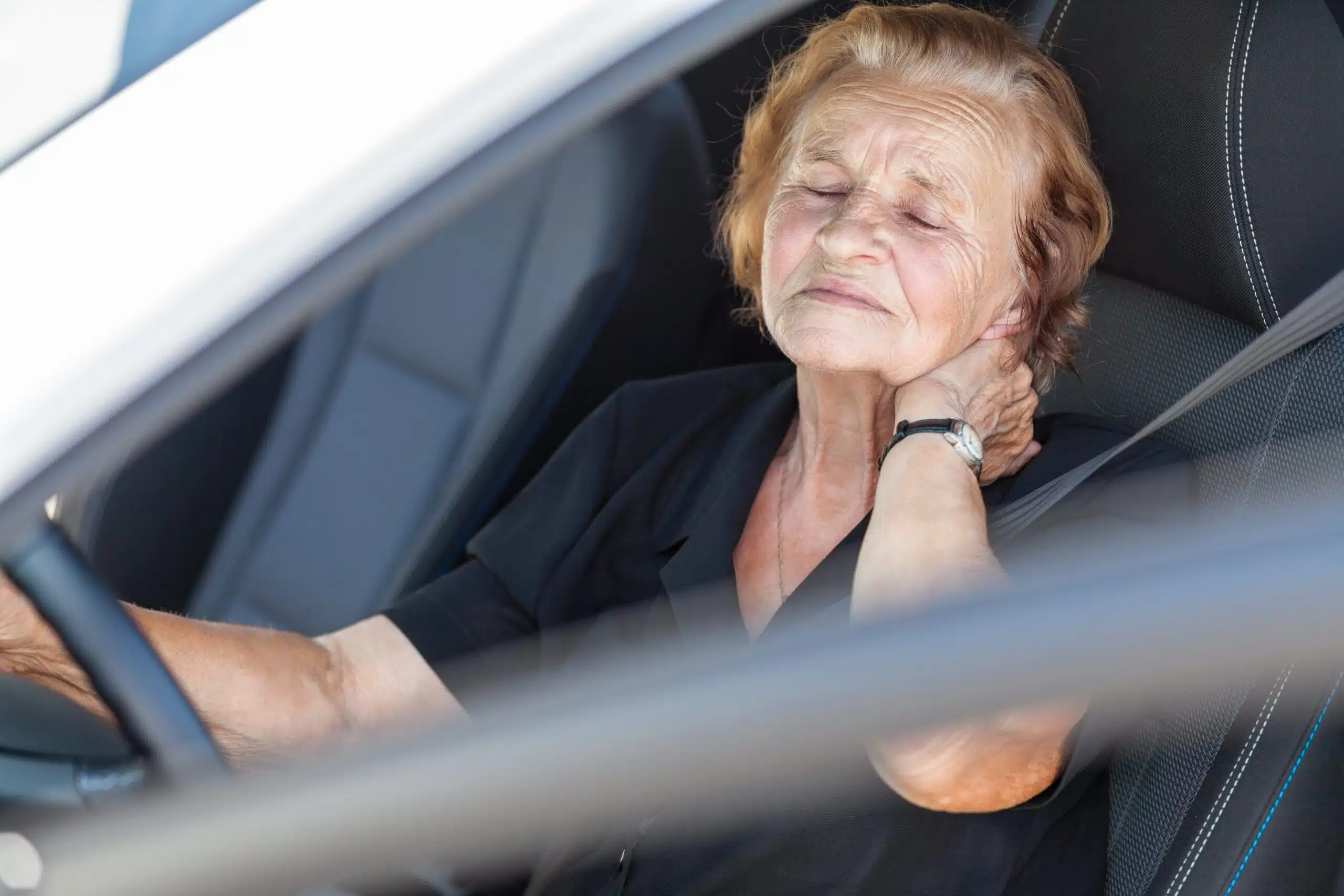 Older woman in driver's seat holding her neck after a car accident
